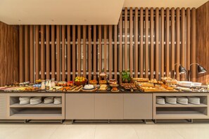 A buffet setup with various food items and a modern wooden wall design. - Laghetto Moinhos (Porto Alegre)