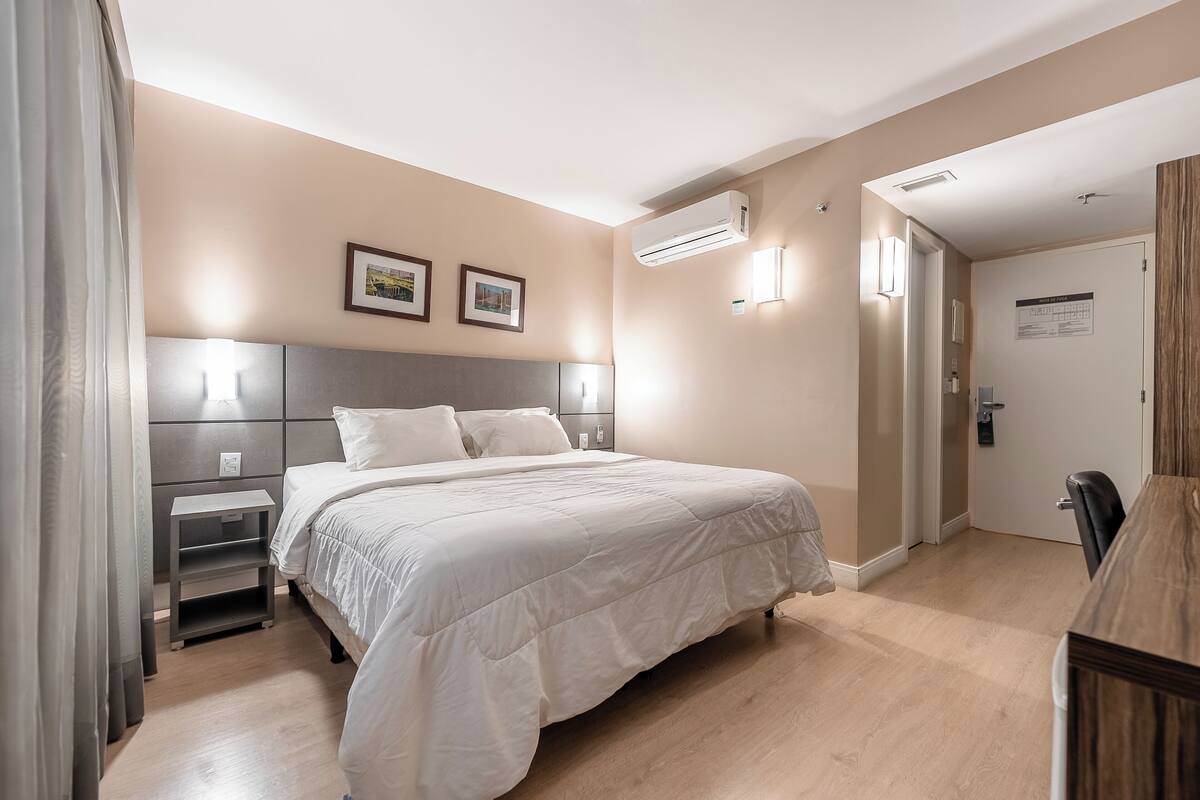 A bedroom with a bed, bedside tables, an air conditioner, and a door.