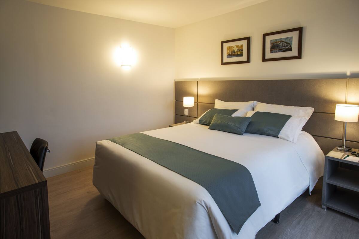 A hotel room with a large bed, bedside tables, a desk, and a chair.