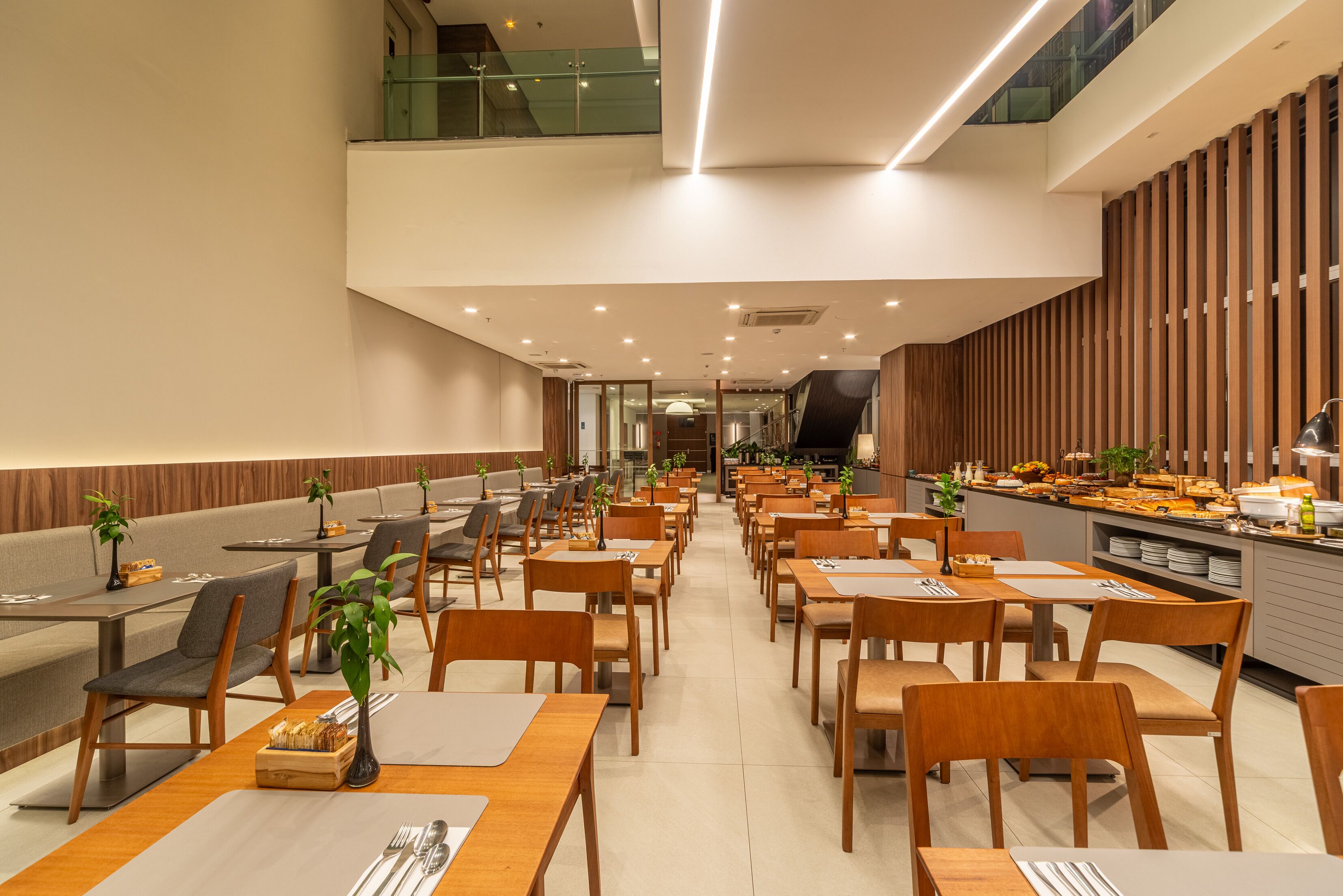A modern dining area with multiple tables and chairs, a buffet counter, and a staircase leading to an upper level.