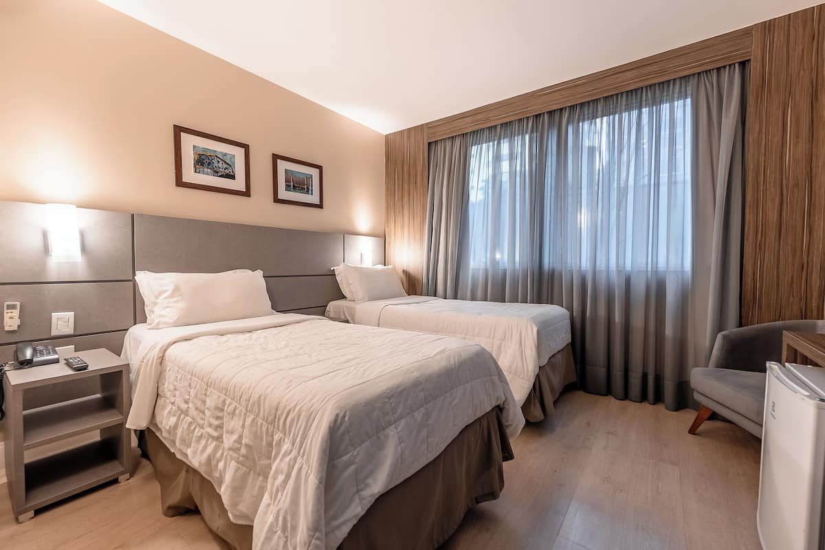A hotel room with two beds, a desk, a chair, and a refrigerator.