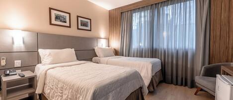 A hotel room with two beds, a desk, a chair, and a refrigerator.