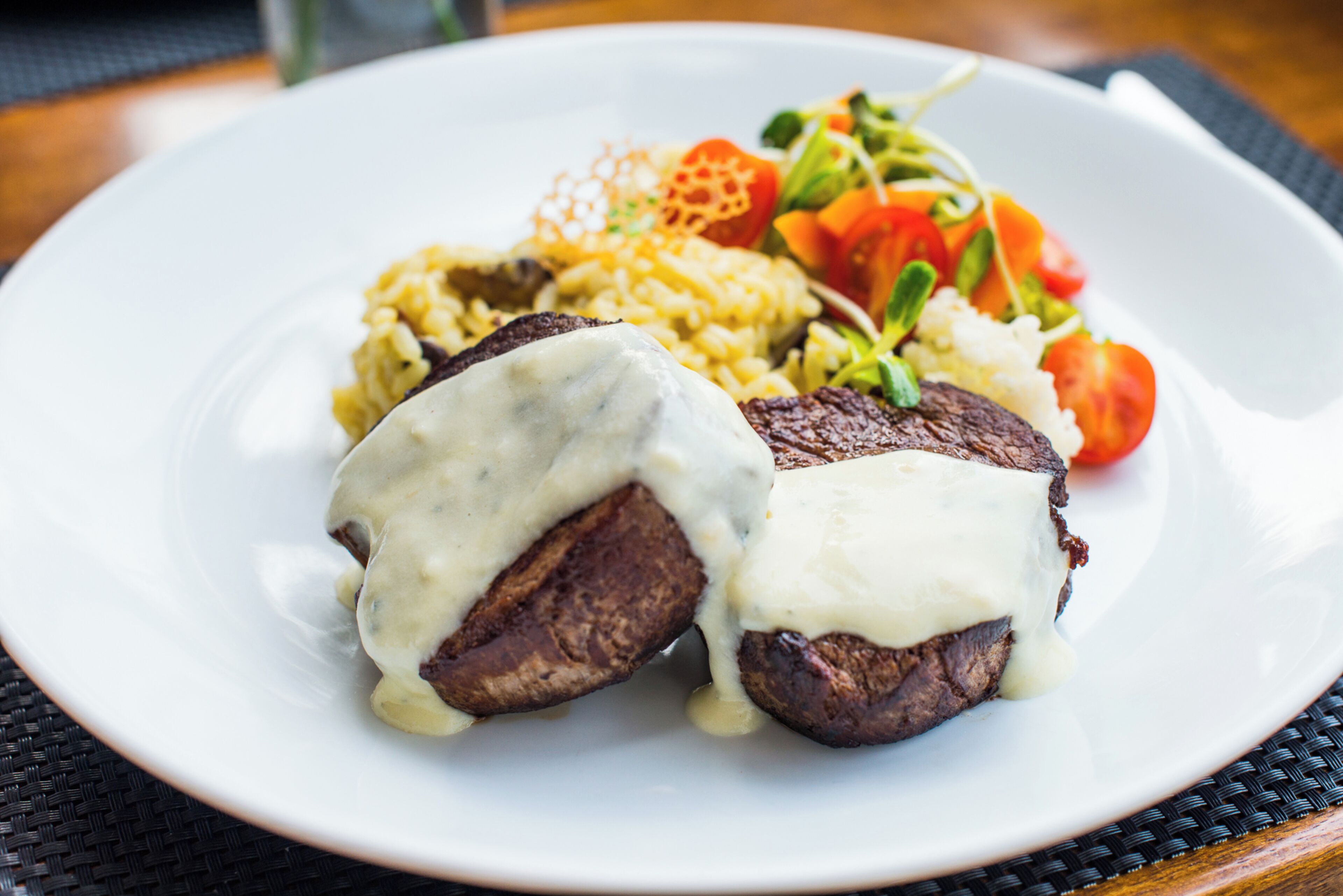 A plate with steak topped with sauce, rice, and a side salad.