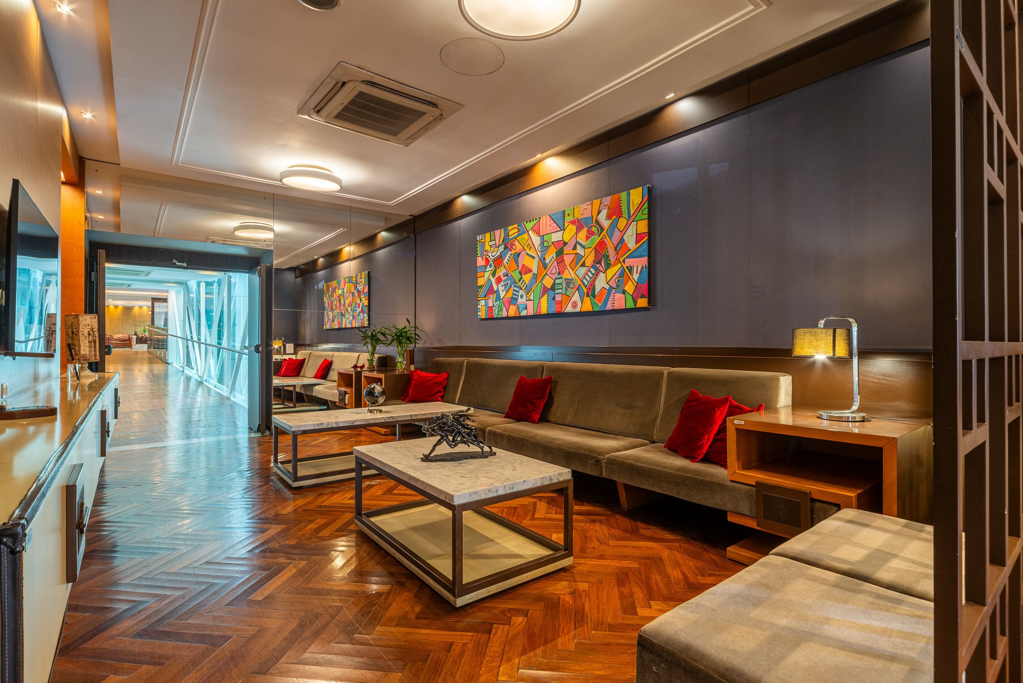 Een hotel lobby met een visgraat parketvloer, een bank met rode kussens, een bijzettafeltje en een schilderij aan de muur.
