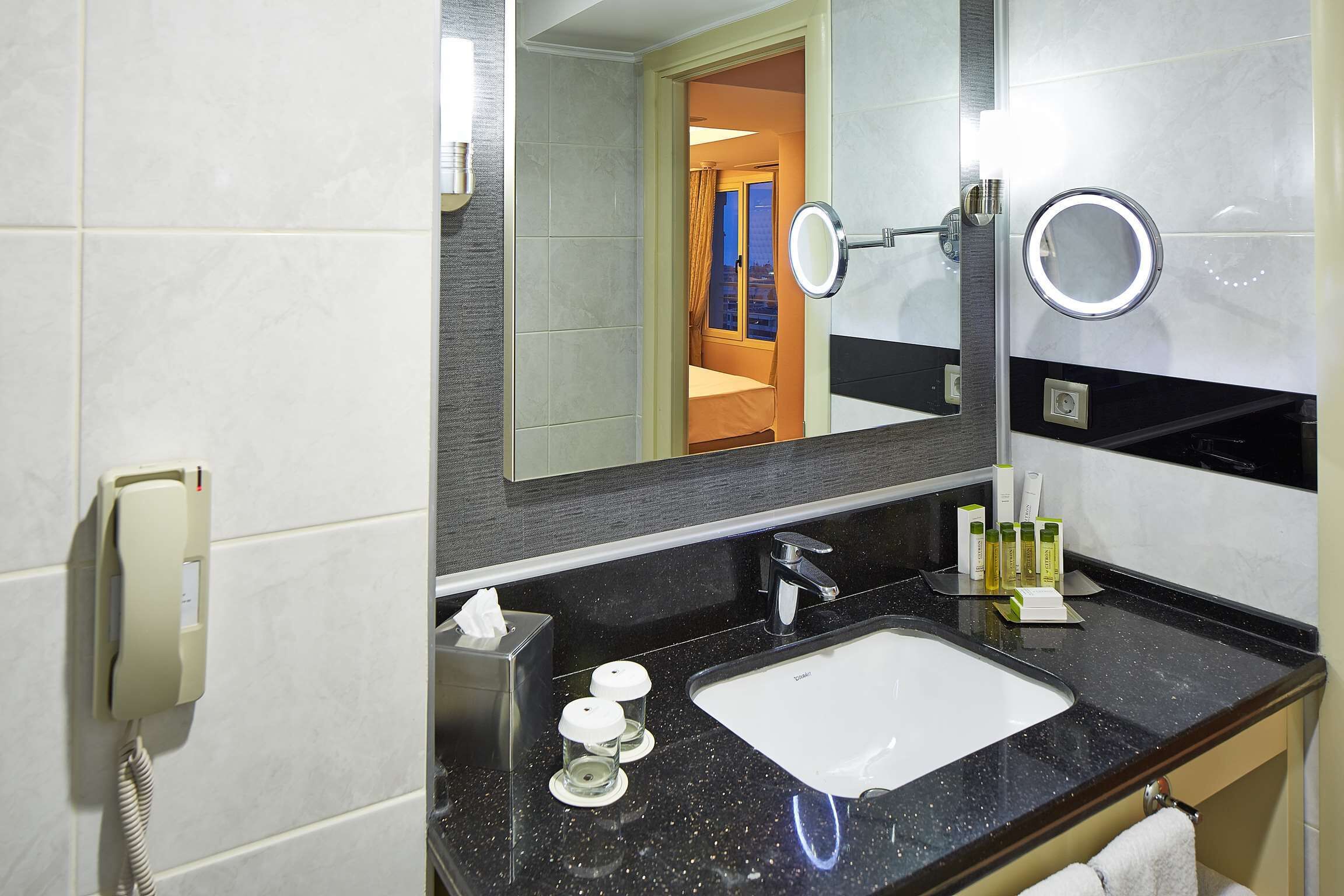 A modern bathroom with a white sink, a large mirror, and a telephone.