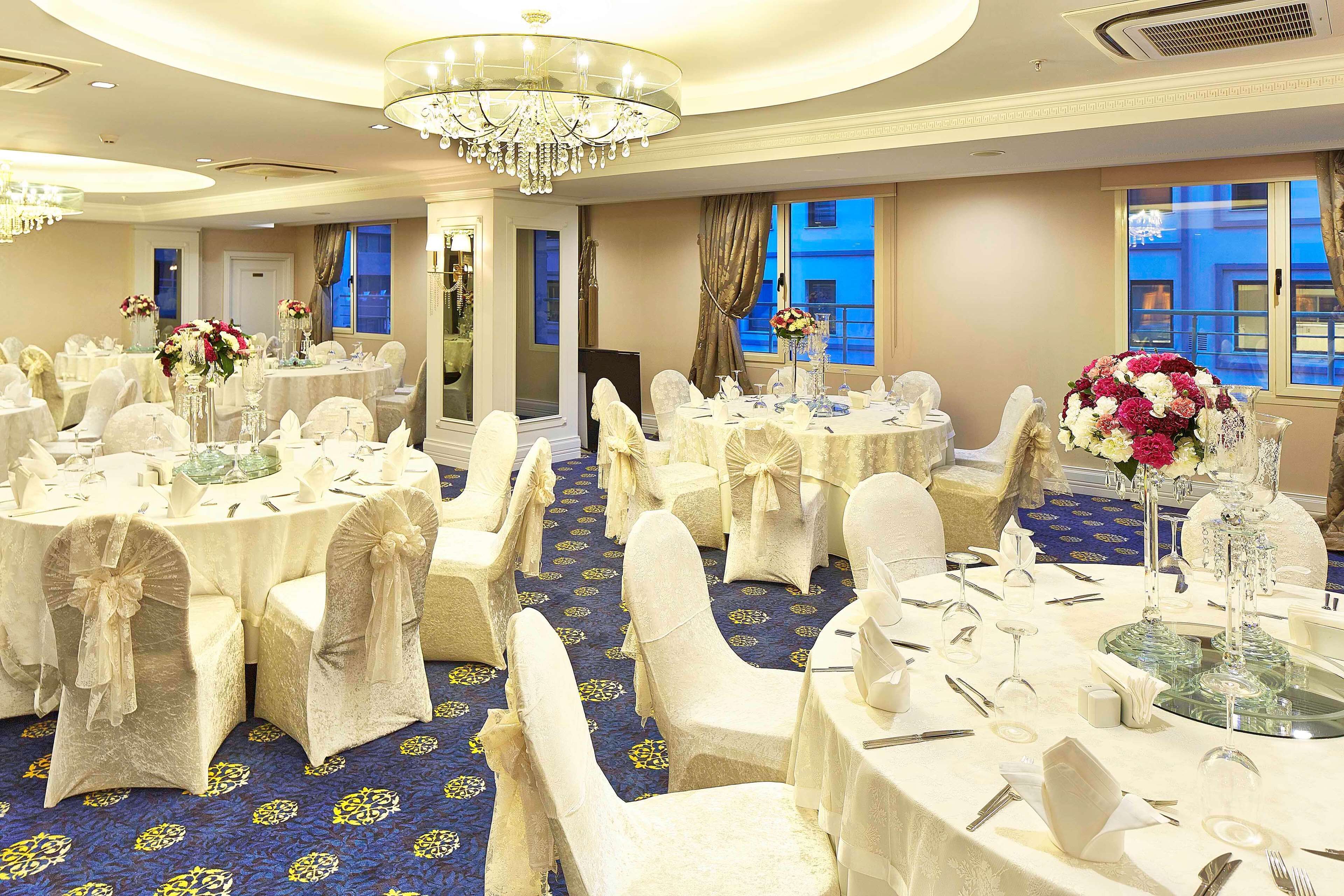 A banquet hall with round tables, white tablecloths, and chairs with white covers.