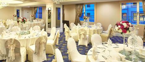 A banquet hall with round tables, white tablecloths, and chairs with white covers.