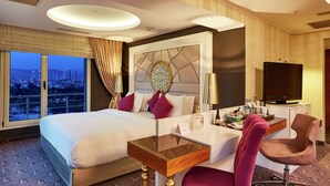 Habitación de hotel con una cama grande, un escritorio con silla, televisión y vistas a la ciudad desde la ventana.
