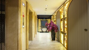 Un pasillo con suelo de madera, una planta grande en maceta con flores moradas y una puerta cerrada con un diseño texturizado.