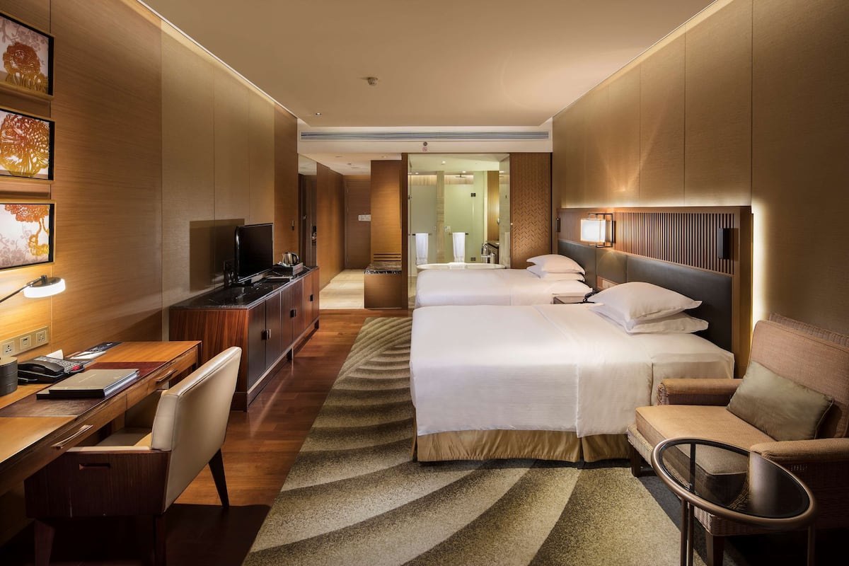 A hotel room with a bed, a desk, a chair, a TV, and a bathroom visible through an open door.