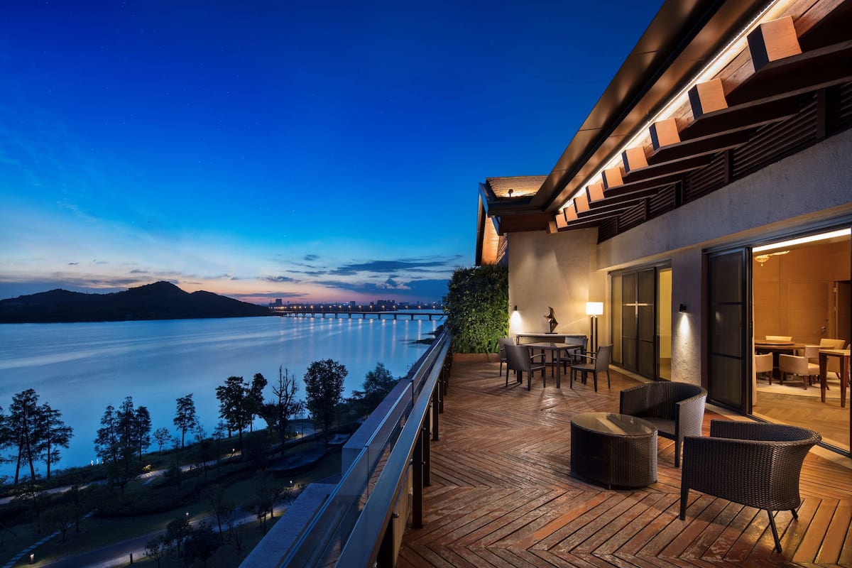 A waterfront balcony with outdoor seating, a view of the water, and a distant cityscape.