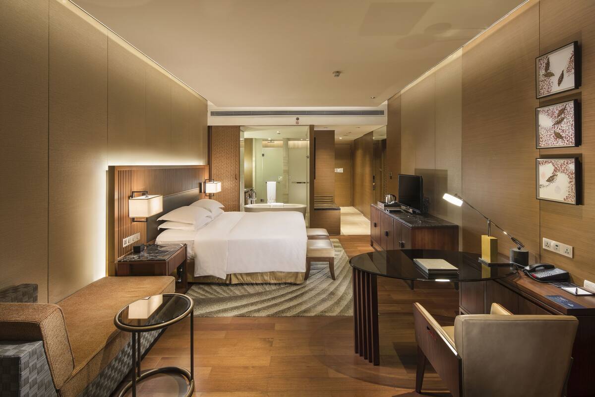 A modern hotel room with a bed, desk, and seating area.
