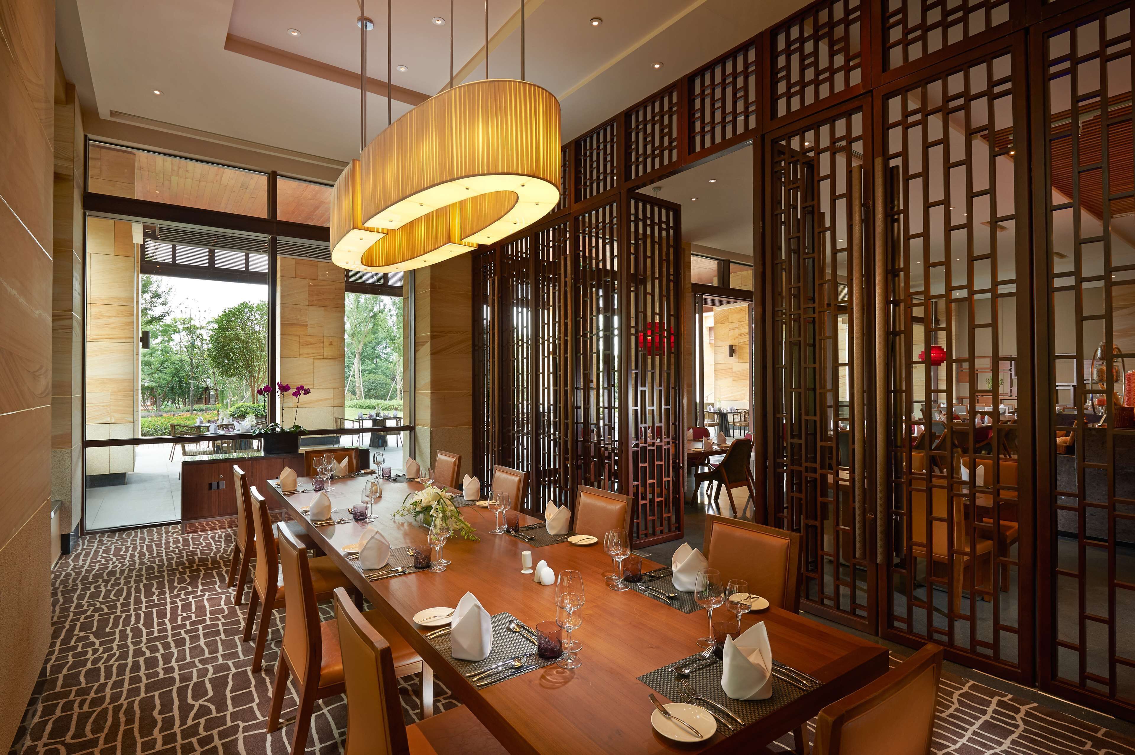 A dining area with a long wooden table set for a meal, surrounded by chairs, with a large hanging light fixture above.