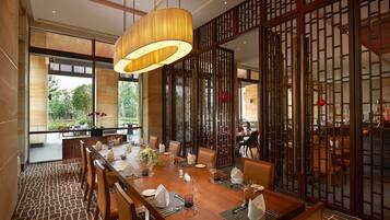 A dining area with a long wooden table set for a meal, surrounded by chairs, with a large hanging light fixture above.