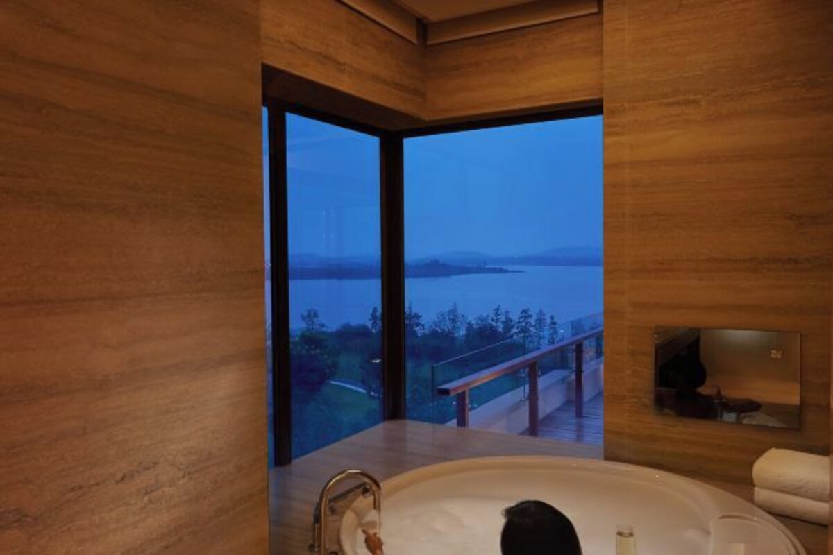 A modern bathroom with a large bathtub, wooden walls, and a view of a body of water and a bridge.