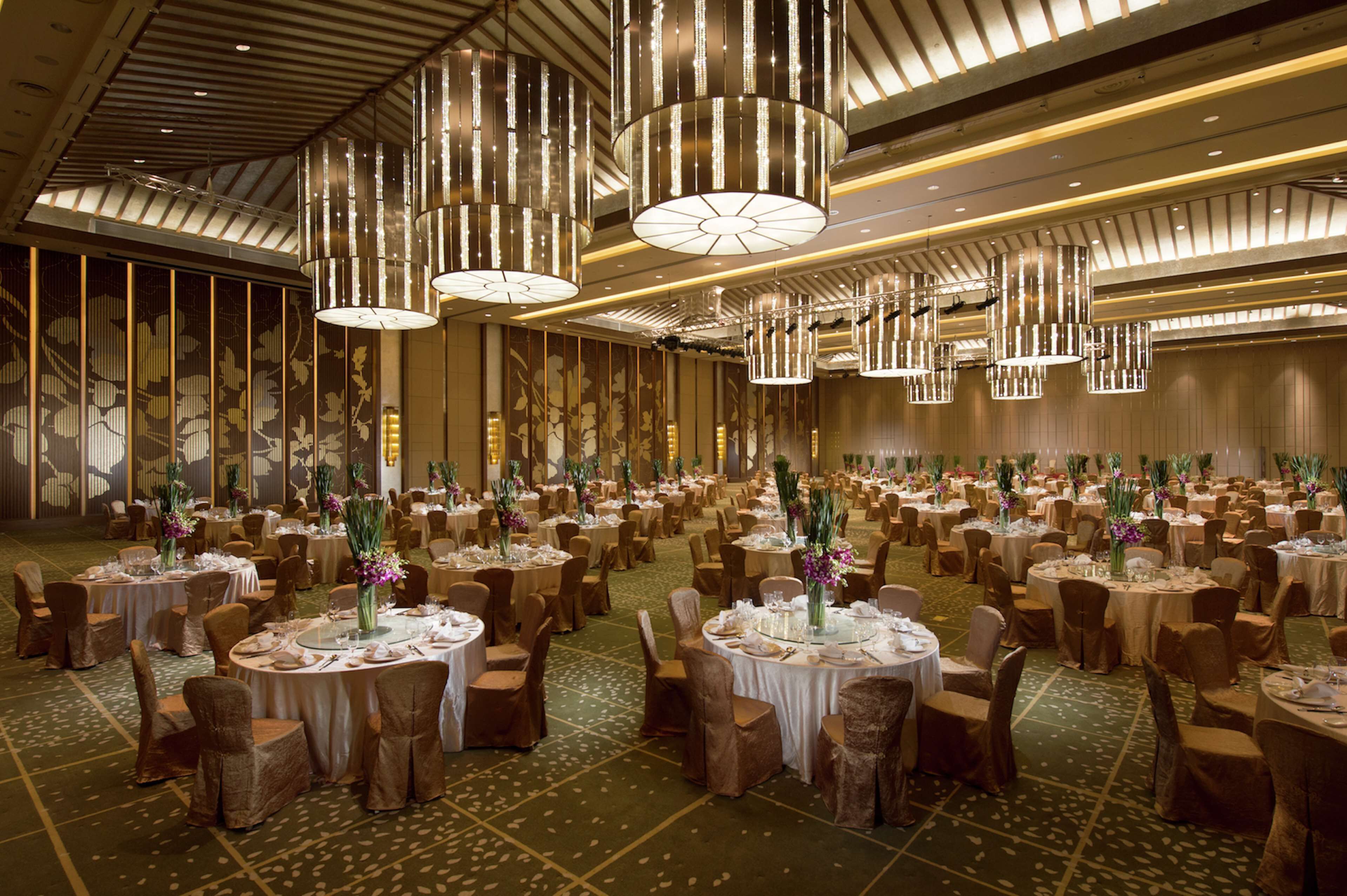 A banquet hall with round tables, chairs, and hanging chandeliers.