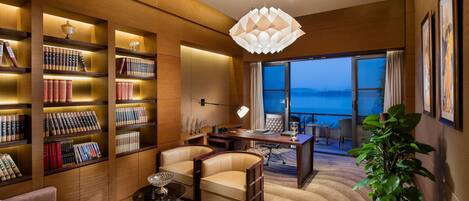 Habitación de hotel moderna con una amplia estantería, sillones de cuero, zona de comedor y vista al mar.