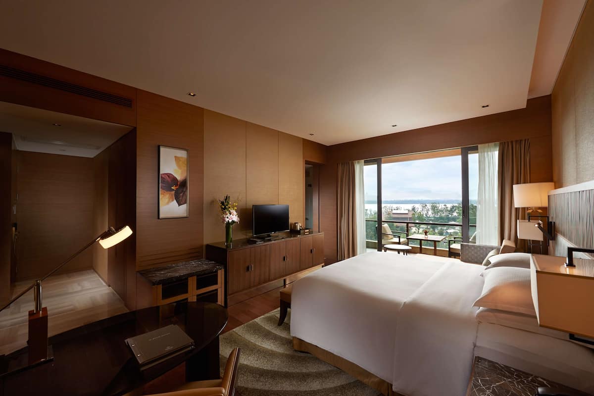 A hotel room with a large bed, a desk with a TV, a chair, a small table, and a view of the city.