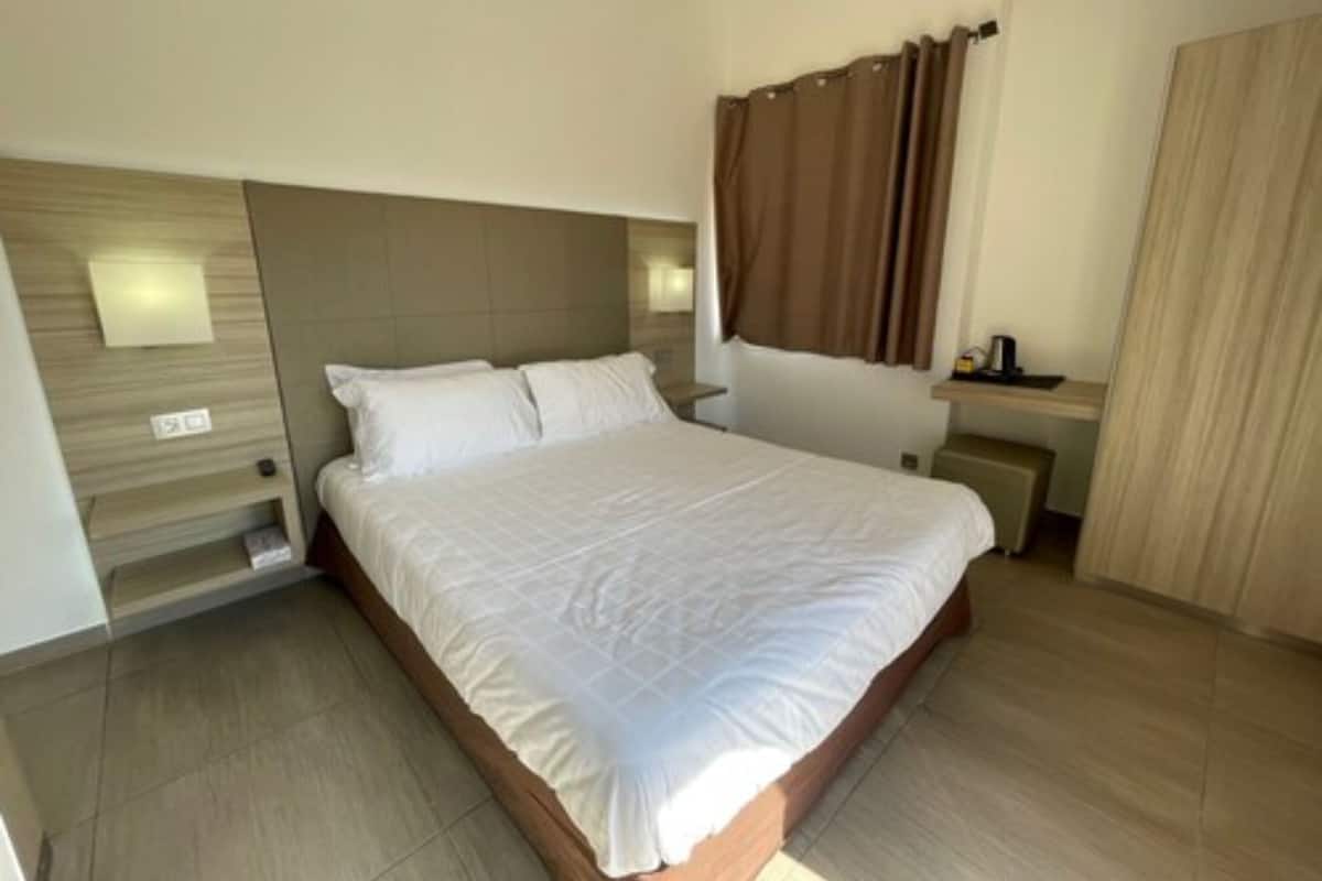 A modern hotel room with a large bed, a wooden headboard, a bedside table, and a small desk with a chair.