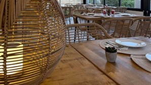 A modern dining area with wicker furniture, large windows, and pendant lighting. - Hôtel L'Escale Coté Port (L'Île-Rousse)