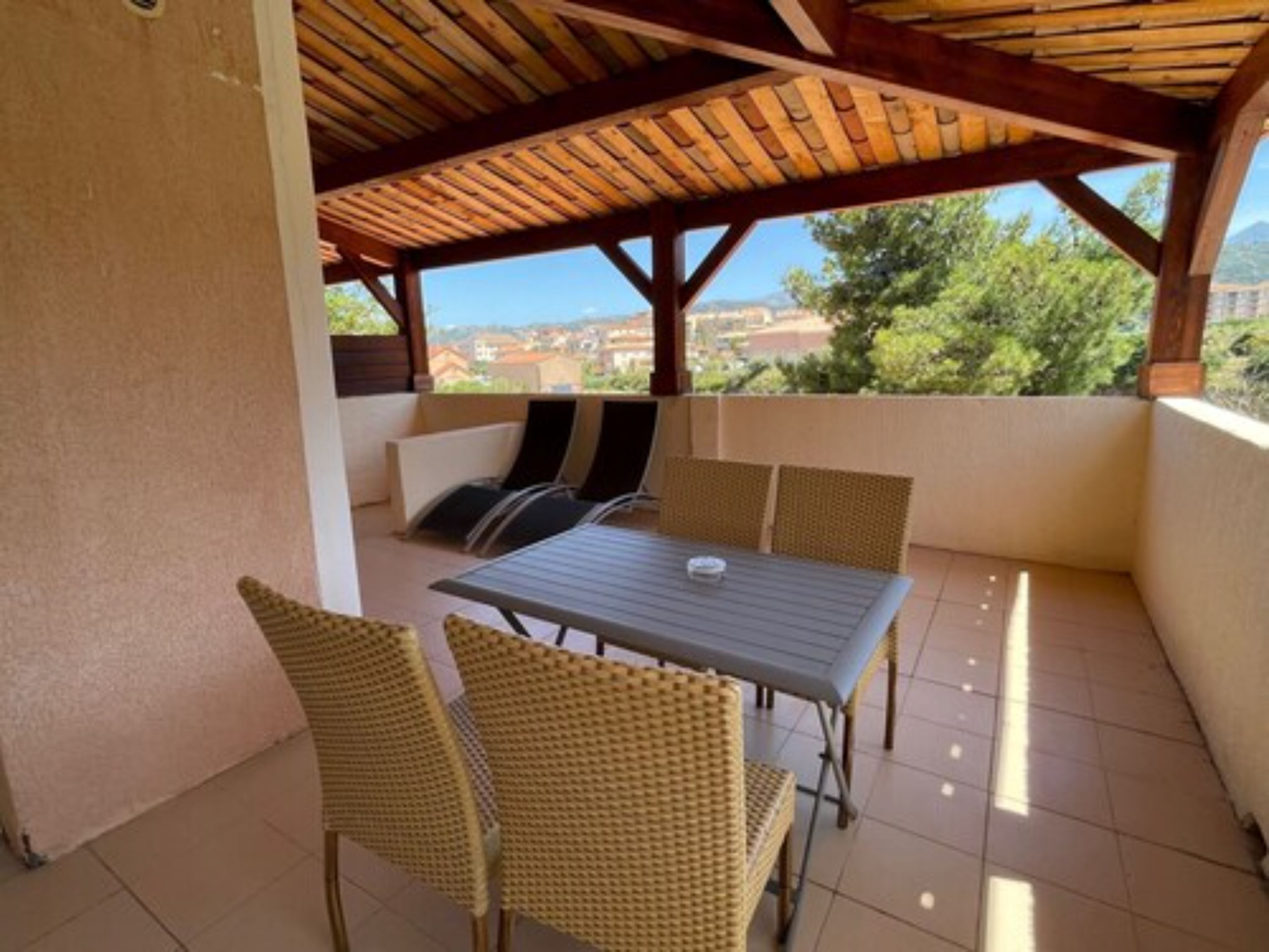 A covered patio with a table and chairs, a view of the cityscape, and a tiled floor.