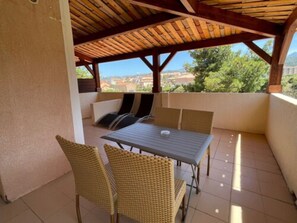 A covered patio with a table and chairs, a view of the cityscape, and a tiled floor.