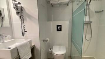 Un baño moderno con ducha envuelta en vidrio, un lavamanos blanco con una toalla y un inodoro.