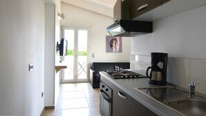 A modern kitchen with a built-in oven, a coffee maker, and a view of the outdoors through a glass door. - Hôtel L'Escale Coté Port (L'Île-Rousse)