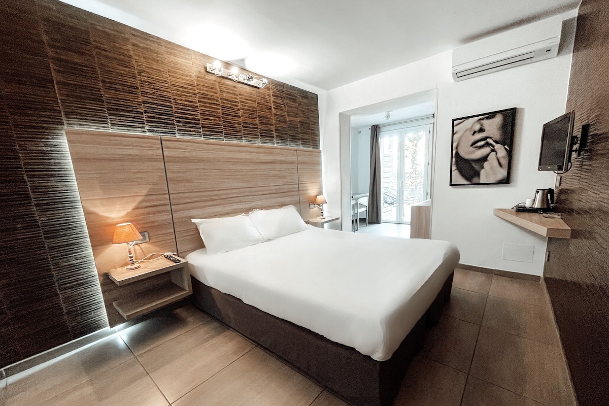 A modern bedroom with a large bed, wooden panel wall, and a view of the outdoors.