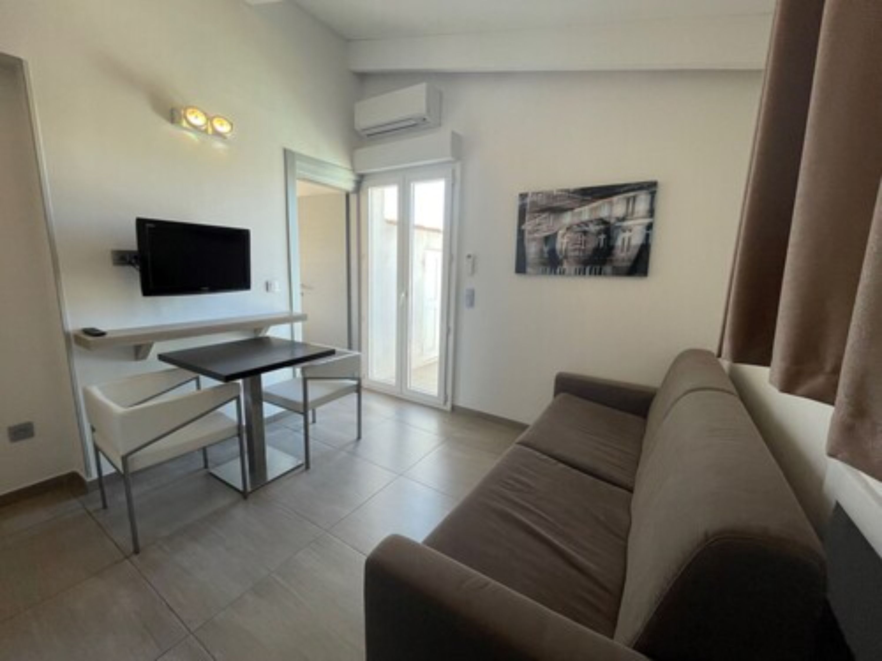 A modern living room with a flat-screen TV, a small table, a sofa, and a painting on the wall.