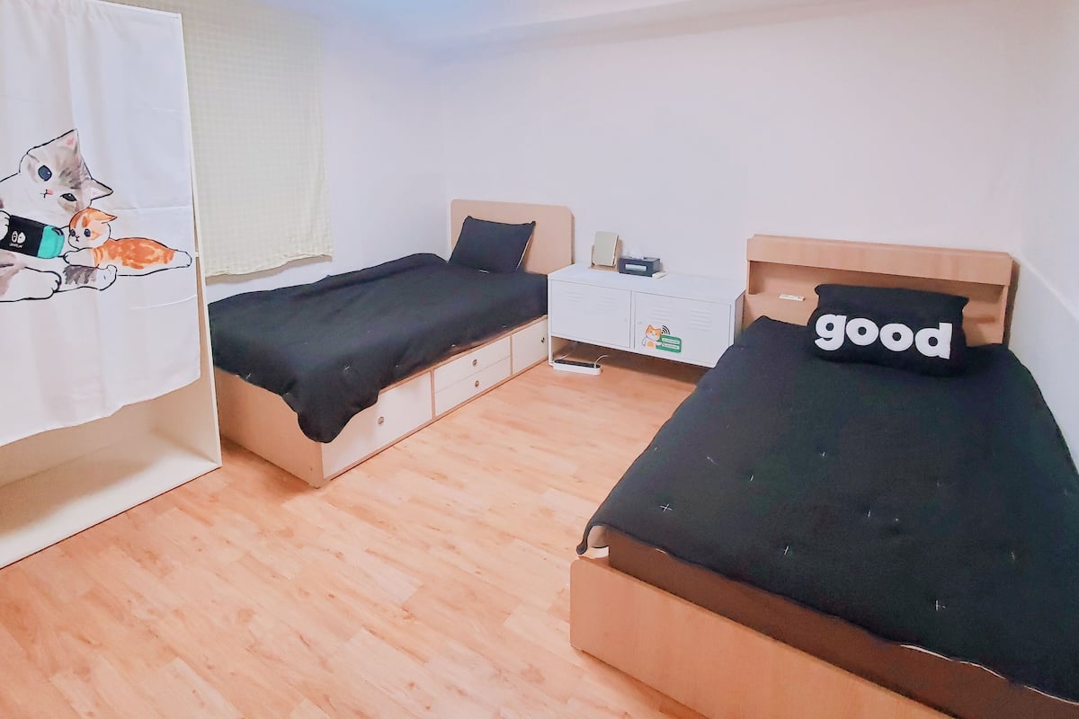A small, well-lit room with two beds, a white wardrobe, and a wooden floor.