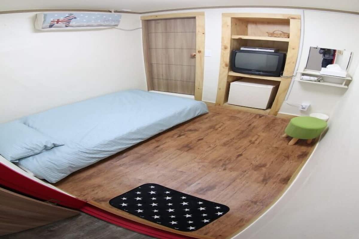 A compact room with a single bed, a small TV, a green stool, and a wooden cabinet.