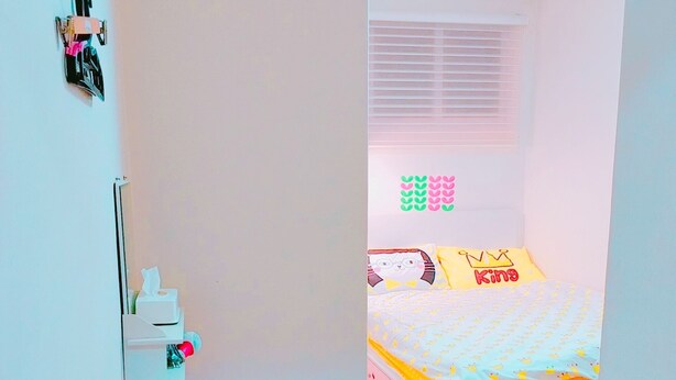 Une chambre à coucher avec un lit, un petit tabouret, une armoire blanche et une fenêtre avec des stores.