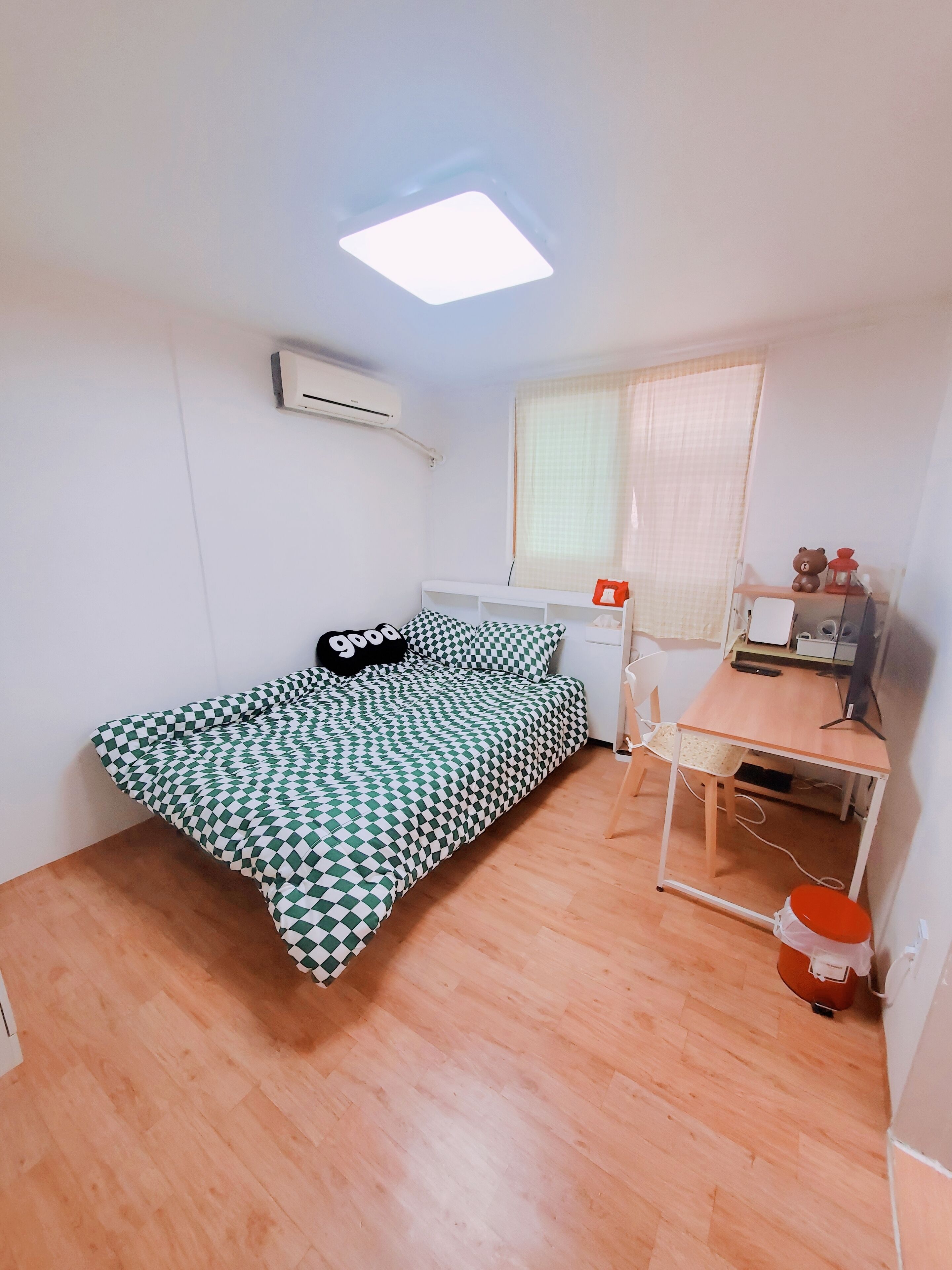 A small, well-lit room with a bed, a desk, and a window.