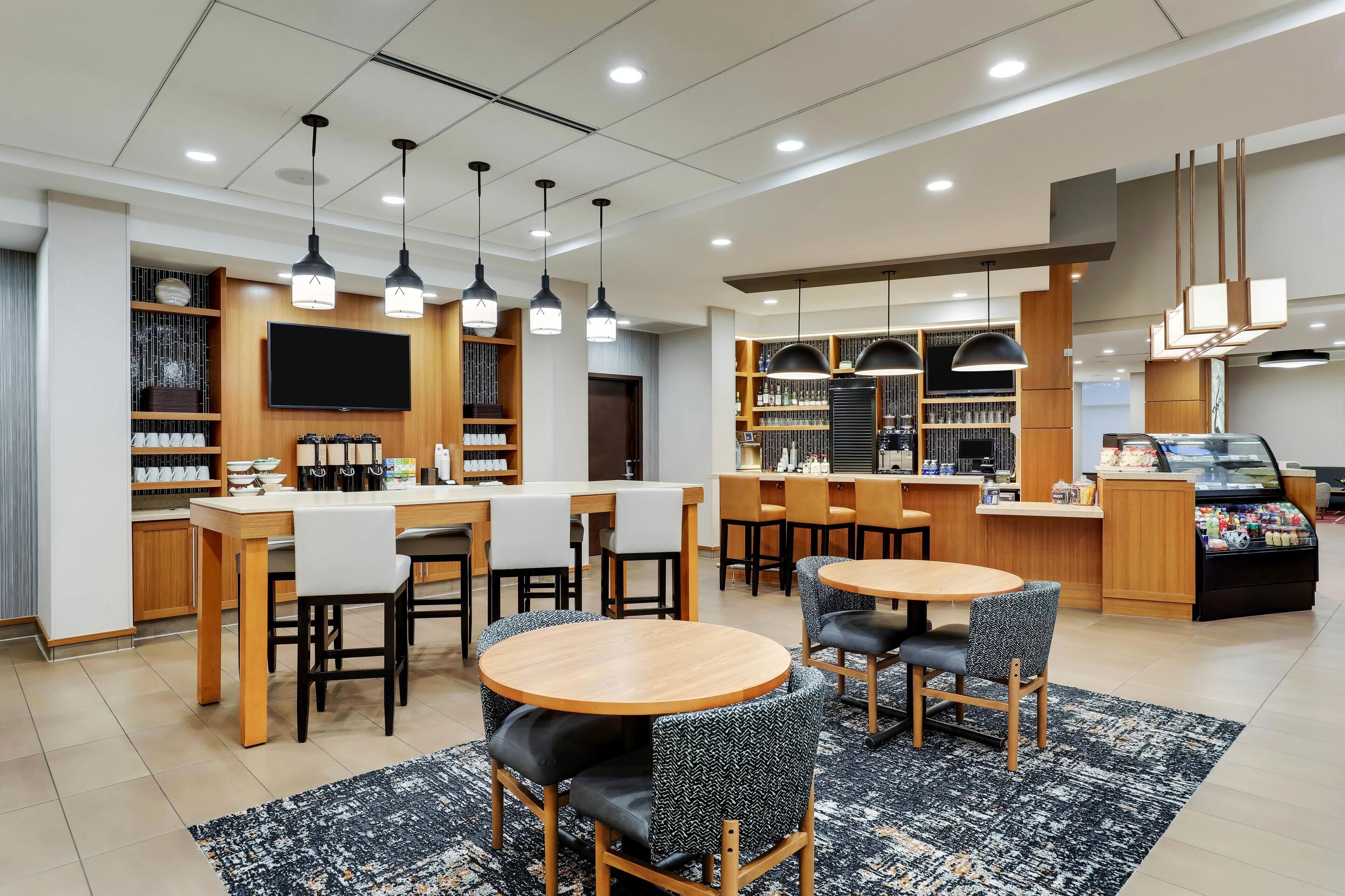 A modern hotel lobby with round tables, bar area, and a TV mounted on the wall.