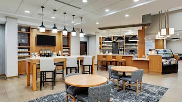 A modern hotel lobby with round tables, bar area, and a TV mounted on the wall.