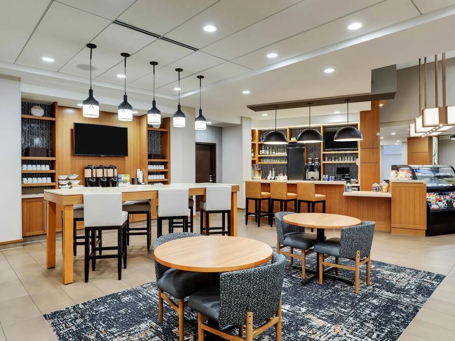 A modern hotel lobby with round tables, bar area, and a TV mounted on the wall.