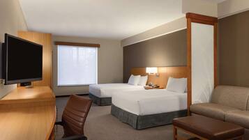 A hotel room with two beds, a desk, a TV, and a sofa.
