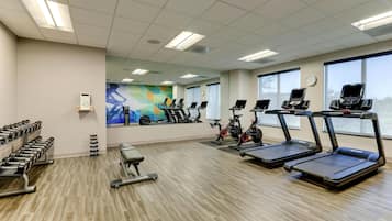 Un gimnasio con cintas de correr, bicicletas estáticas y mancuernas.