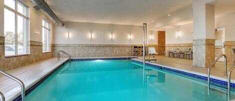 Une piscine avec une terrasse carrelée, une pièce baignée de lumière offrant une vue agréable et un espace détente avec des fauteuils.