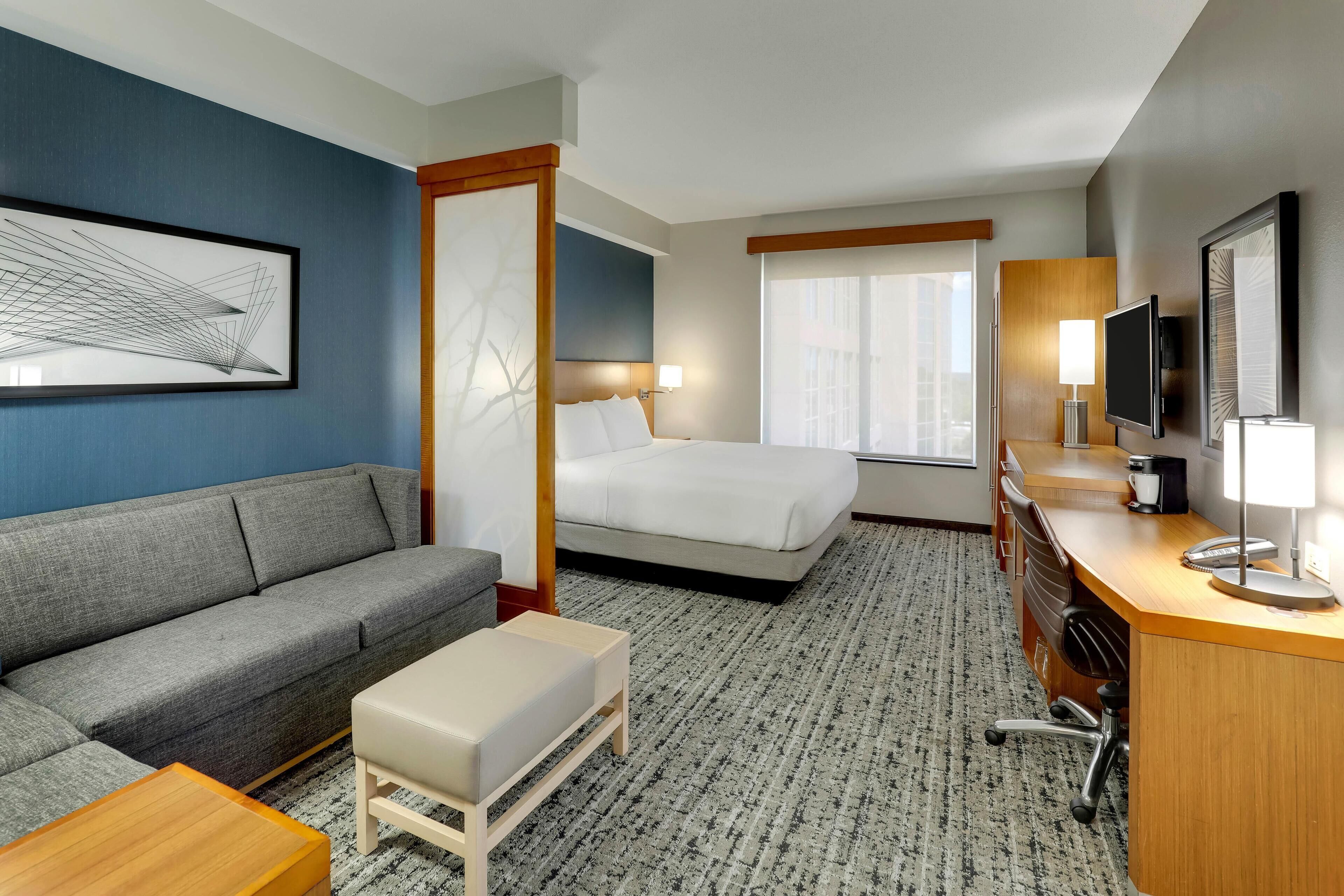Habitación de hotel con sofá, cama, escritorio, televisor y obras de arte en las paredes.