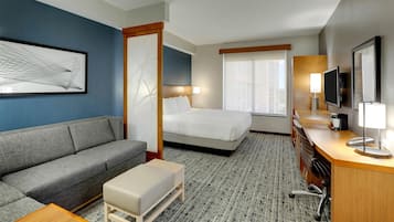 Habitación de hotel con sofá, cama, escritorio, televisor y obras de arte en las paredes.