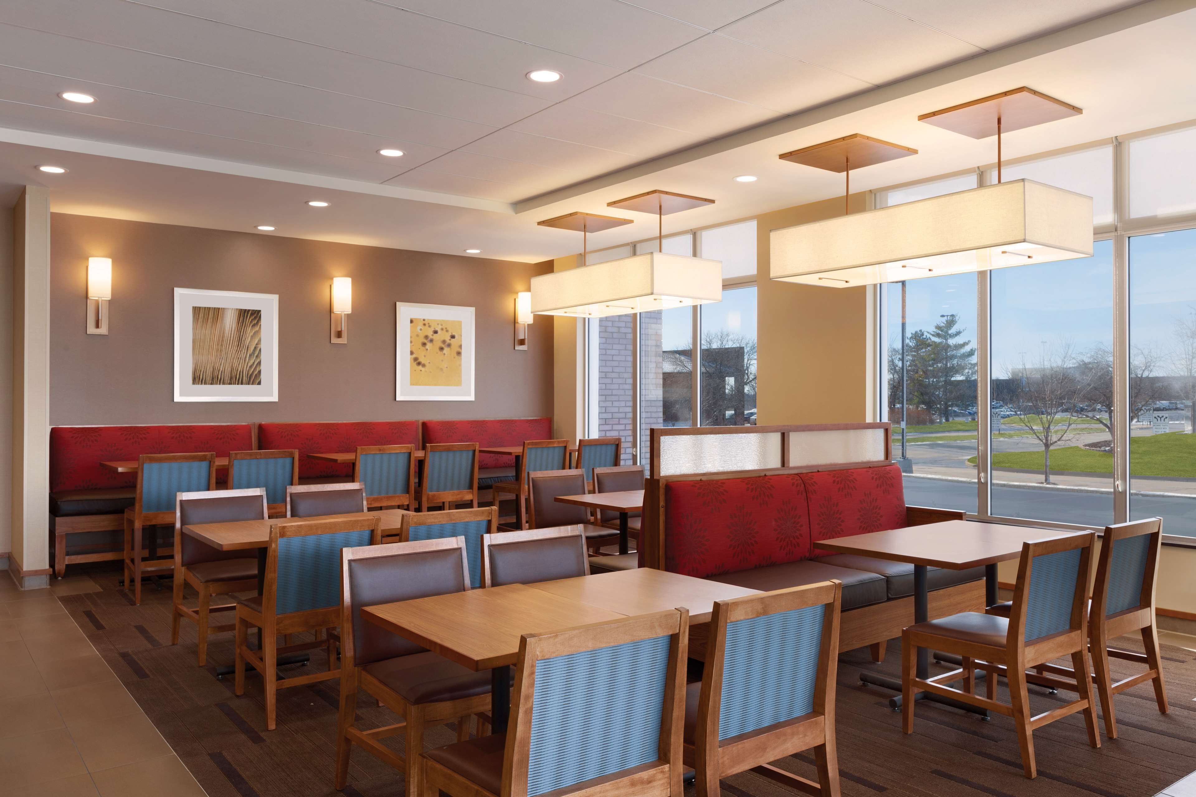 A restaurant with booths and tables, wooden chairs, and pendant lighting.