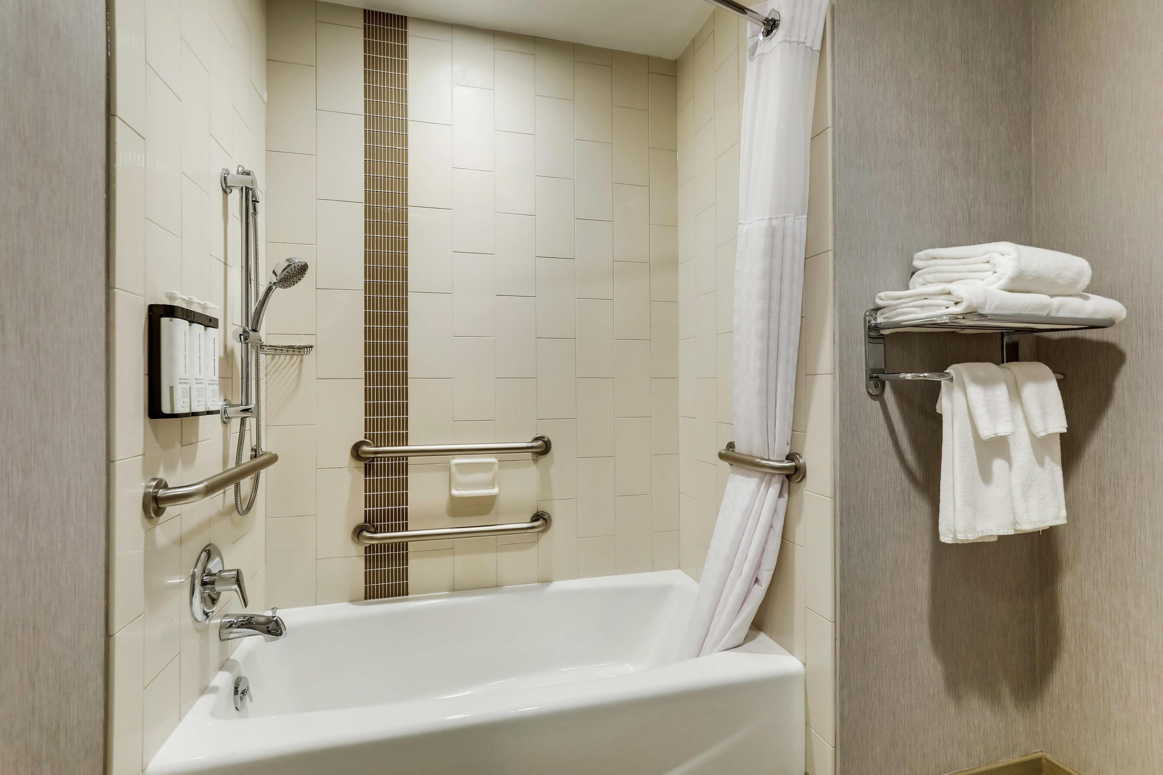 A modern bathroom with a bathtub, shower, grab bars, and a towel rack.