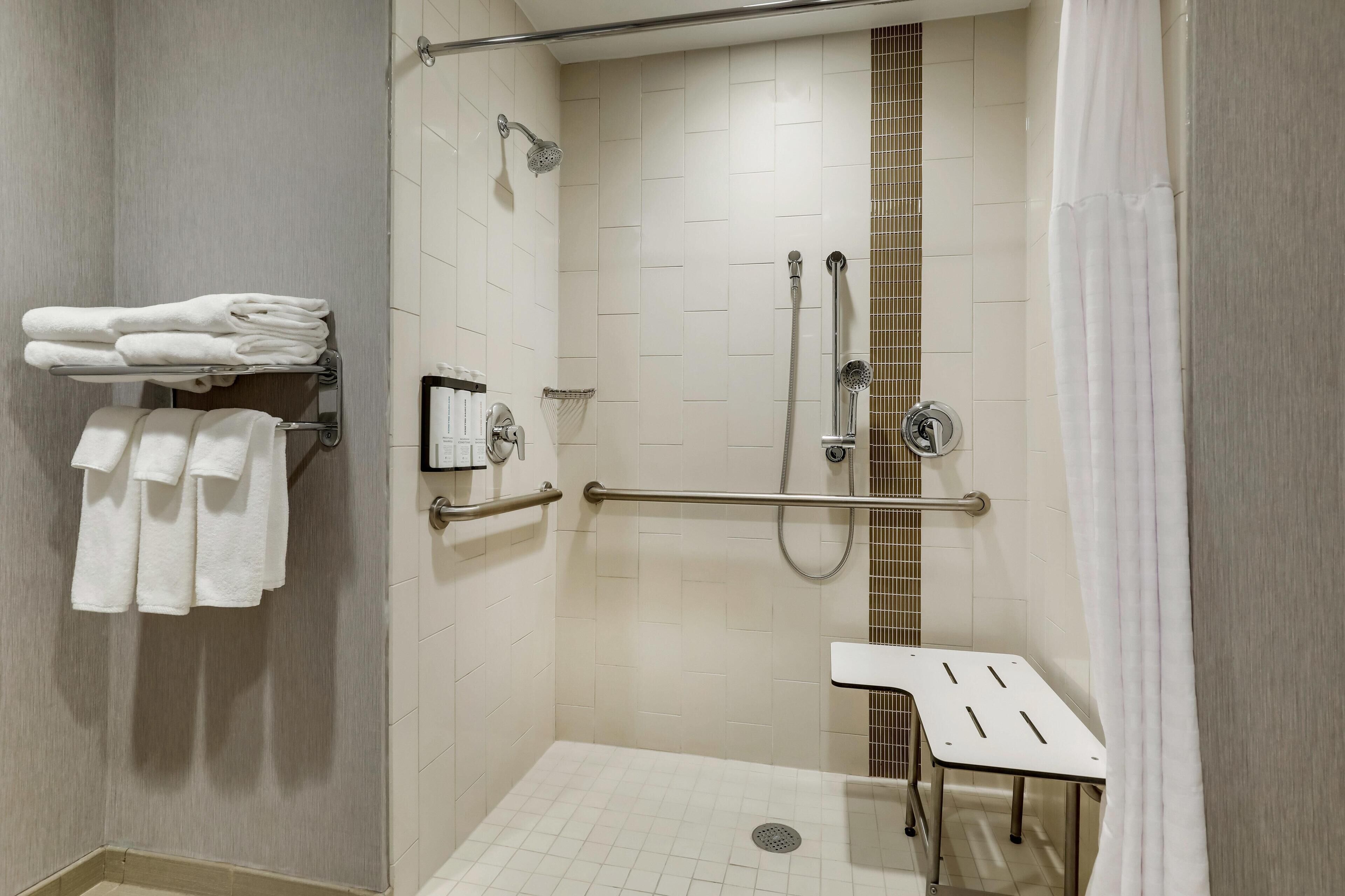 A shower with a grab bar, a white sink, and a towel rack.