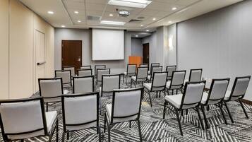 Uma sala de conferências com fileiras de cadeiras, uma tela de projetor e piso coberto de carpete.