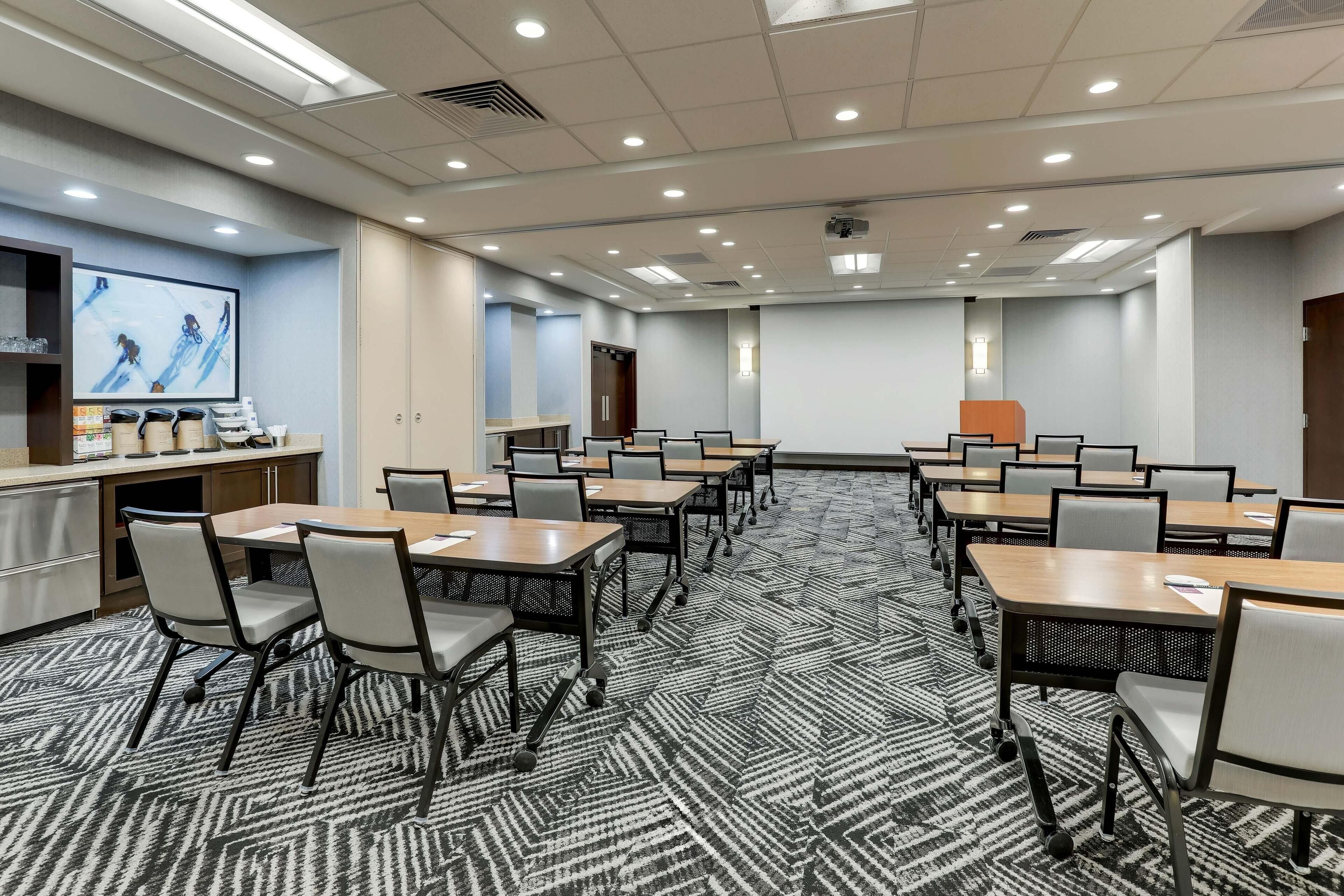 A conference room with multiple tables and chairs, a projector screen, and a presentation area.