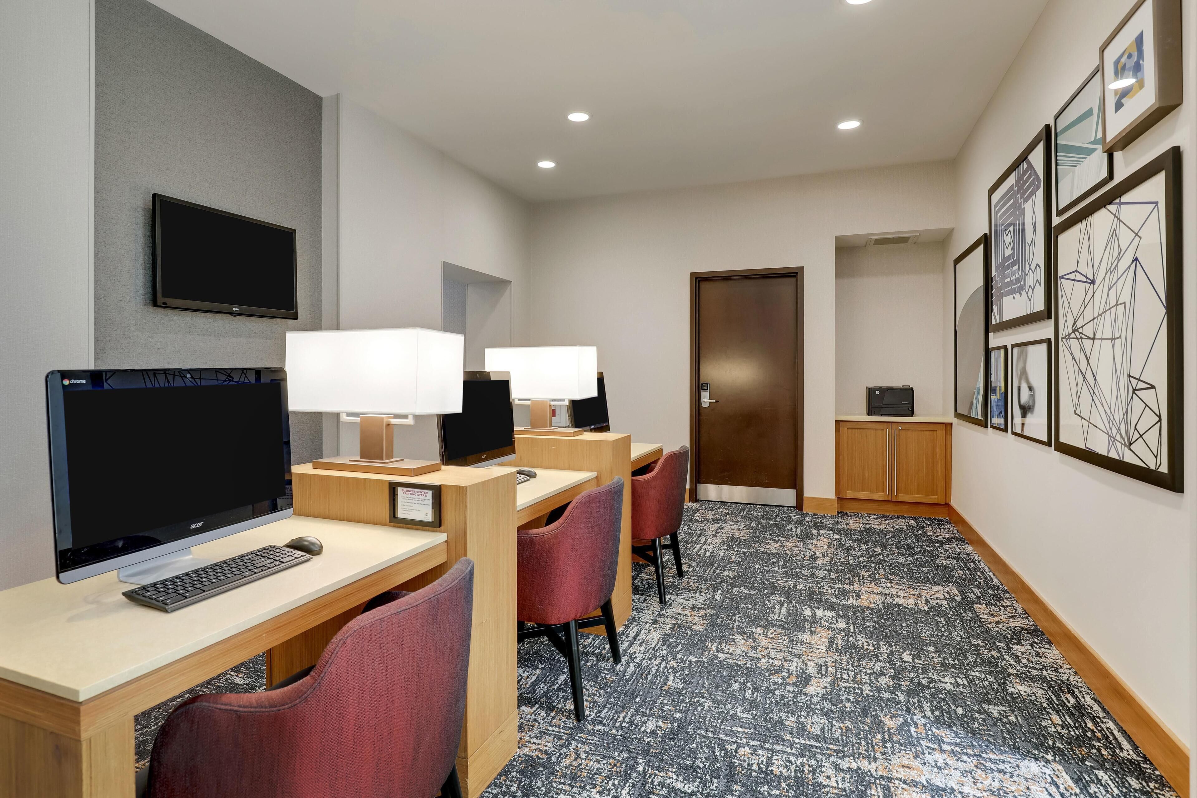 Une chambre d’hôtel équipée d’un bureau, d’un ordinateur, d’une chaise, d’une lampe et d’une œuvre d’art au mur.