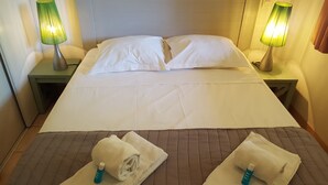 A neatly made bed with white linens, two bedside lamps, and two towels with toiletries on the bed.