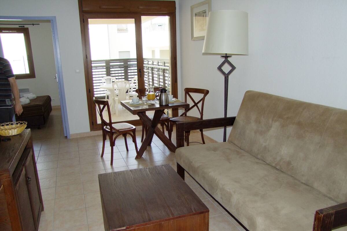 A living room with a sofa, wooden coffee table, and dining area with chairs and a table set for breakfast.